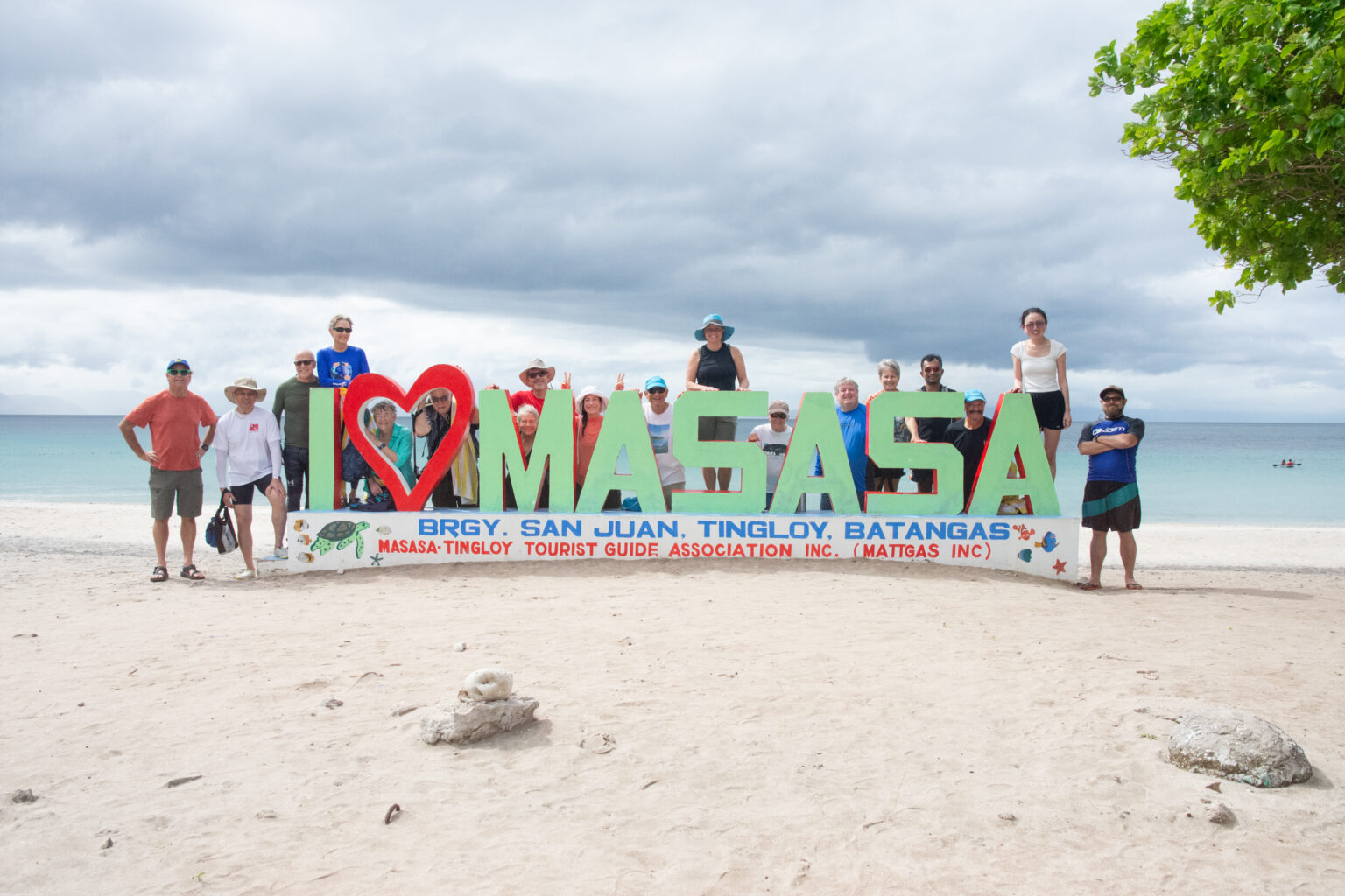 Group of people pose around Masasa Beach sign