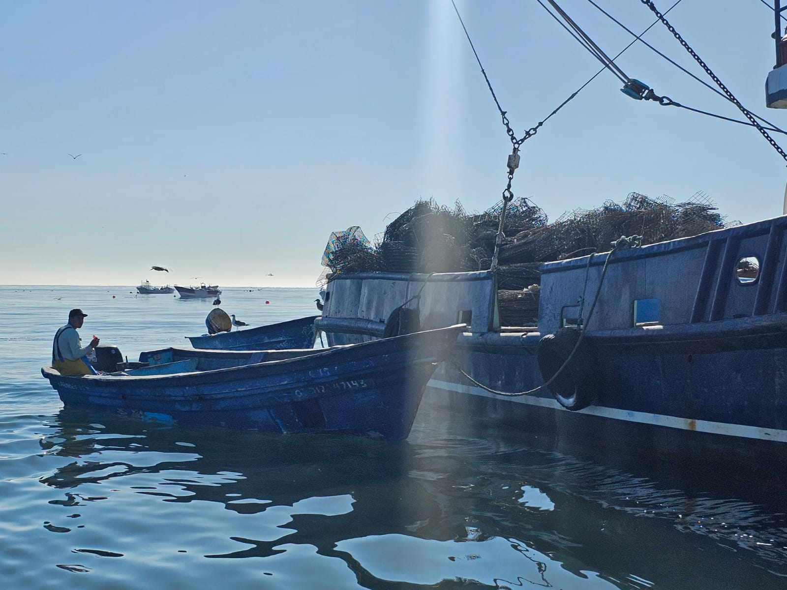 A person sits in a boat next to a barge filled with scrap metal