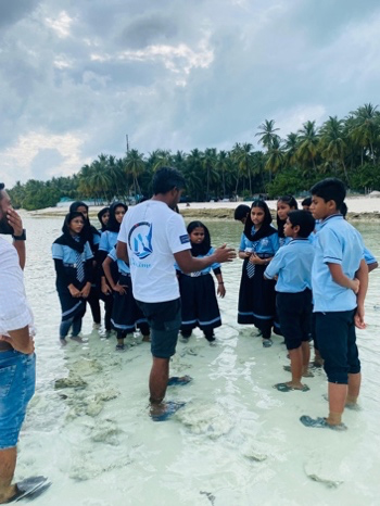 A group of students listens to an instructor while standing in shallow clear ocean water