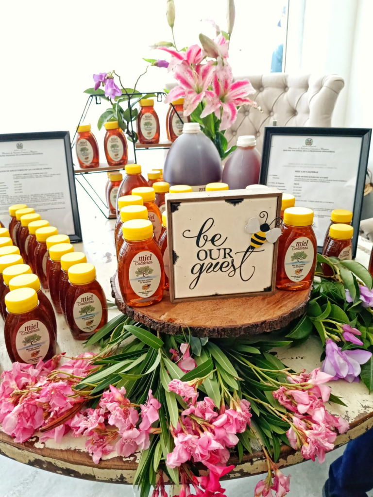 A display of honey and flowers with a sign that says "be our guest"
