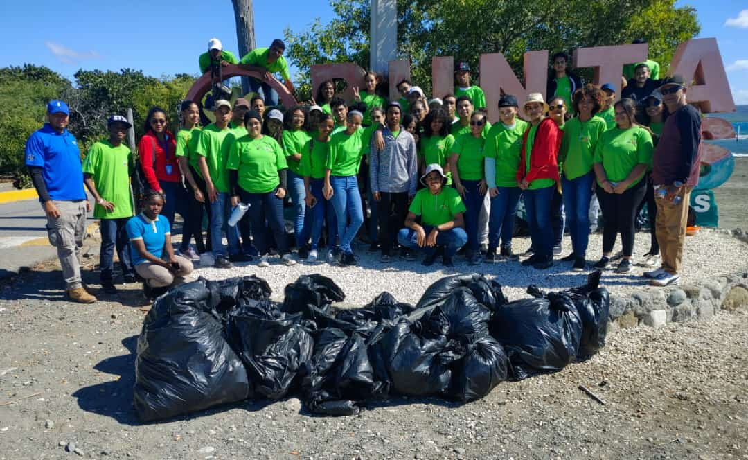 A group of people in green shirts stands with a bunch of full trash bags
