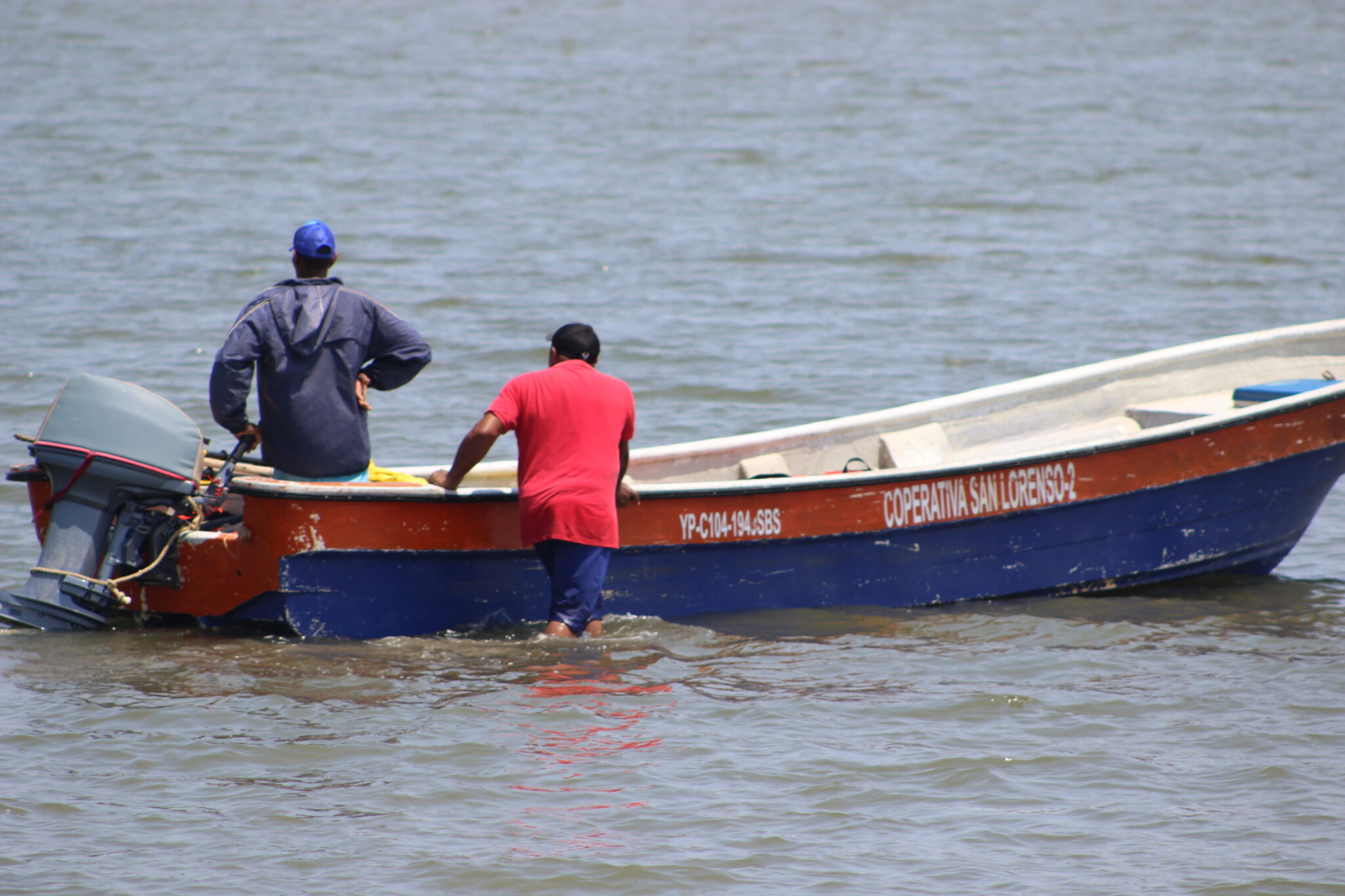 men wading in shallow water with tour boat