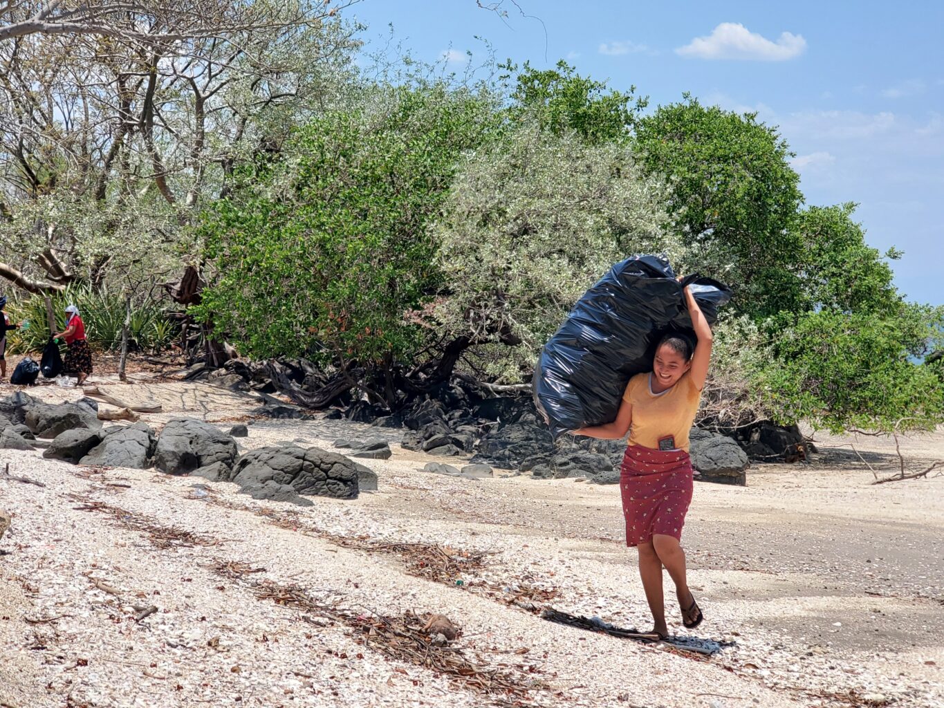 A woman carries a large, full garbage bag