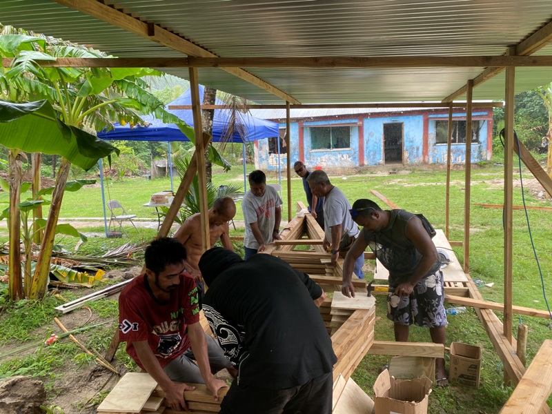 A group of people work with construction materials under a shelter structure