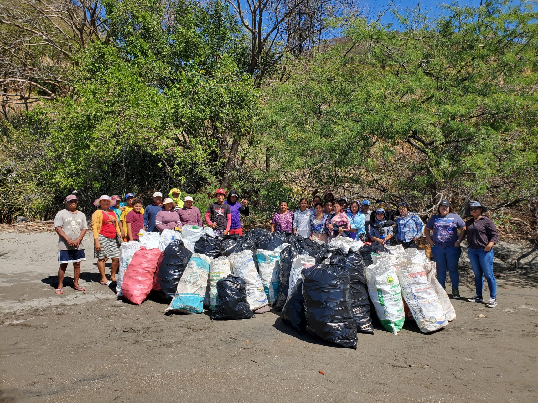 A group of people stand on a beach with many large trash bags