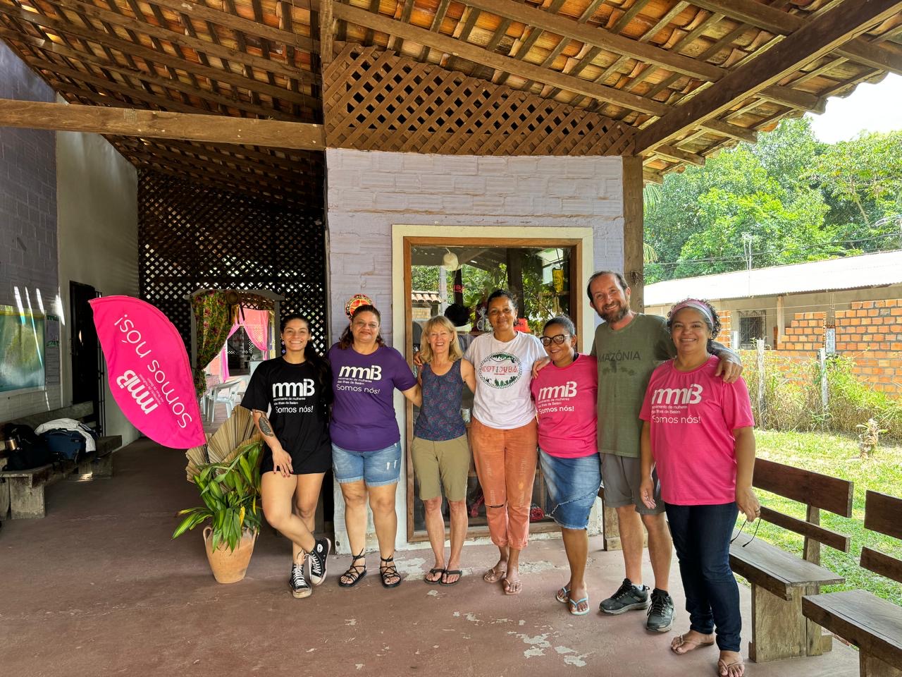 A group of people stands together, some with pink shirts, and a pink banner in the background