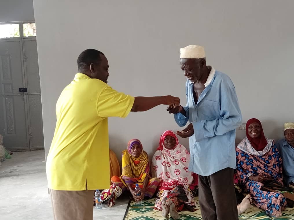 A person in a yellow shirt hands keys to a person in a blue shirt while several other people look on