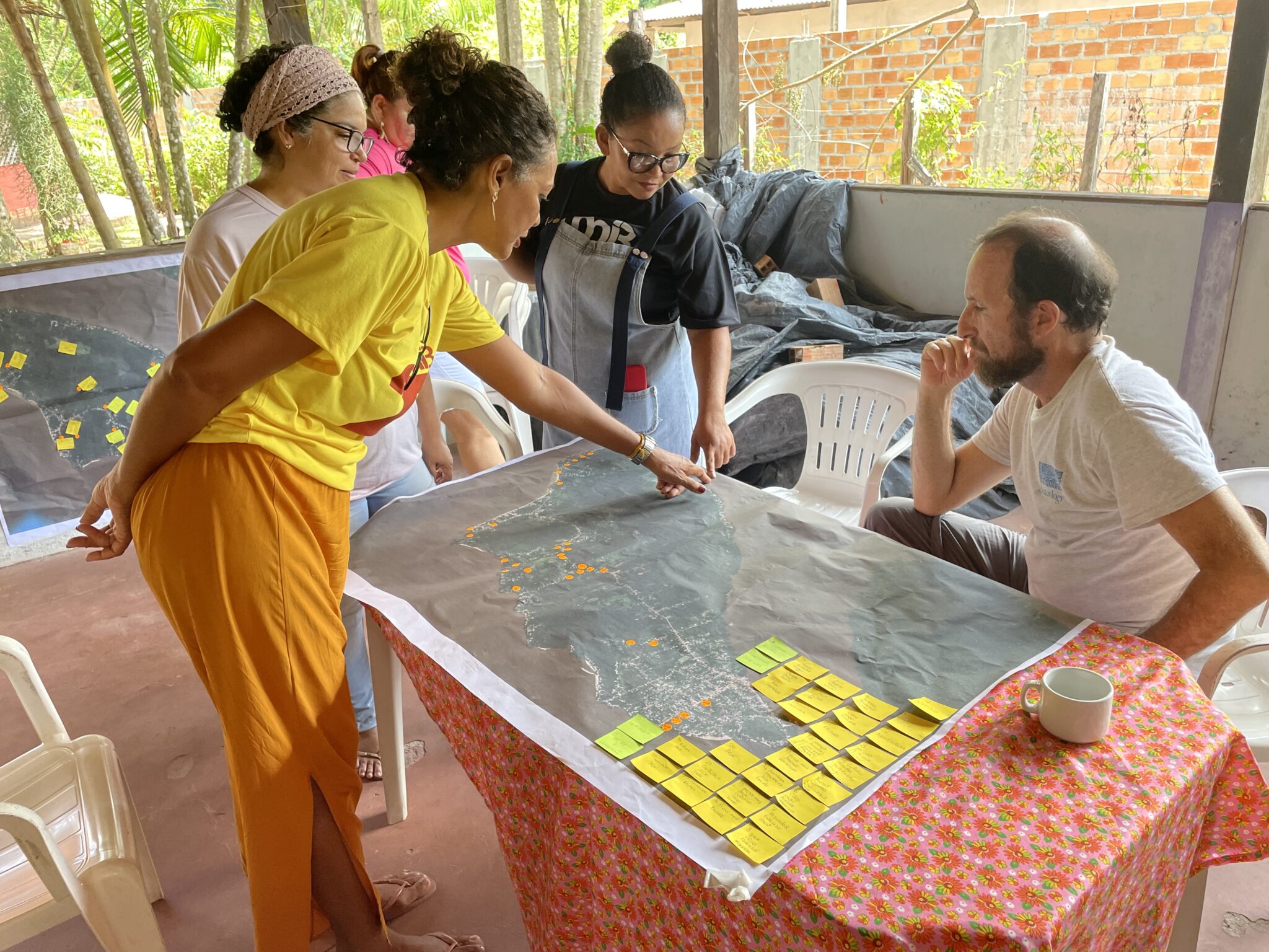 A person in a yellow shirt points at a map on a table while others look on