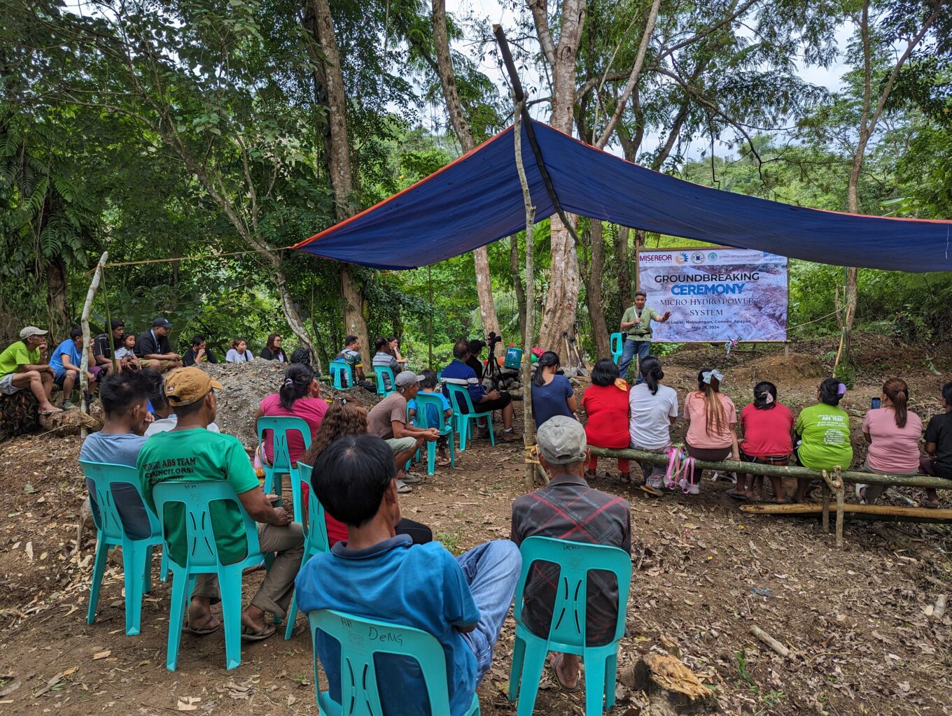 A group of people sit under a tent and watch a presenter