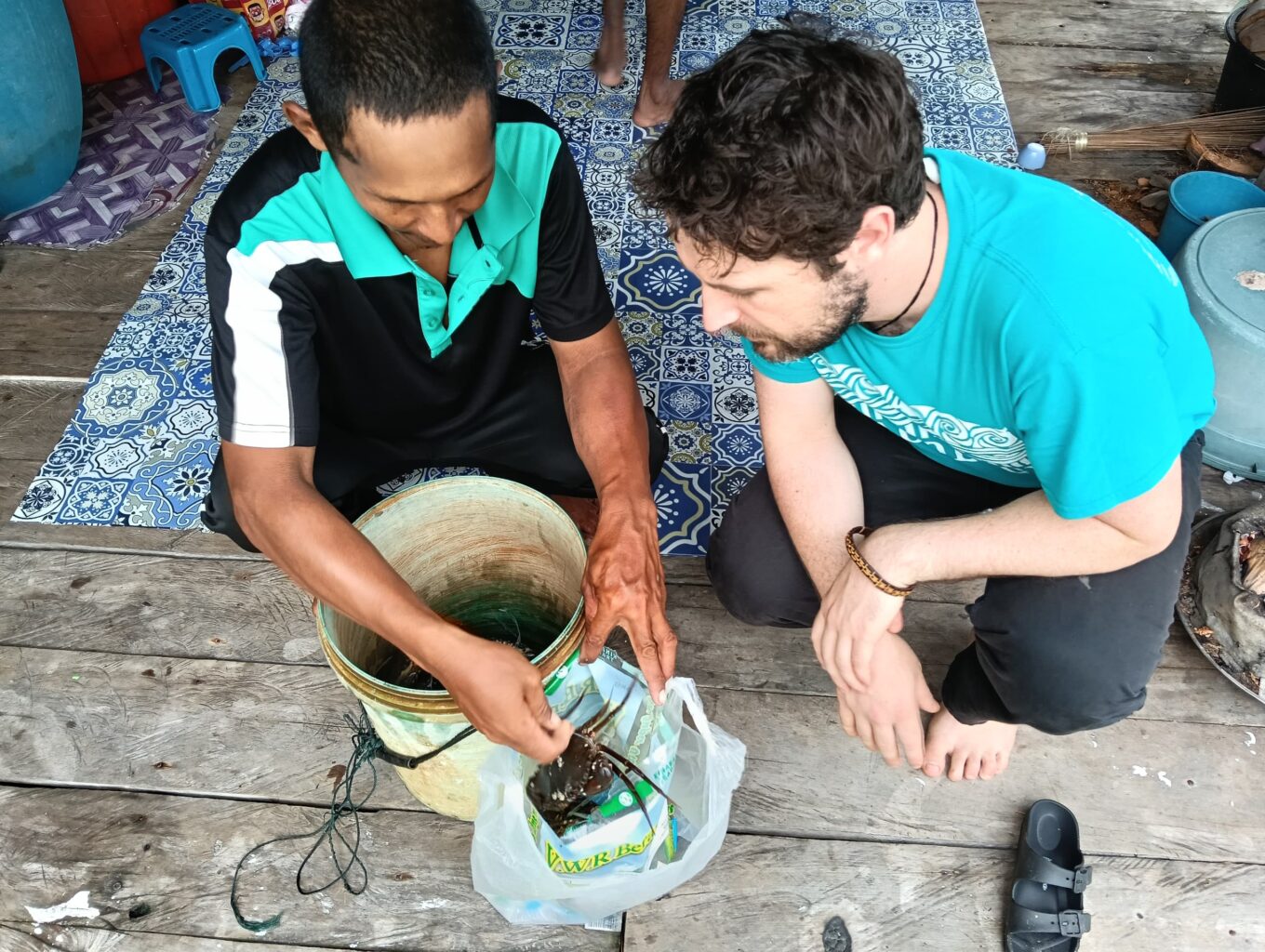 Two men sit on floor examining a crab