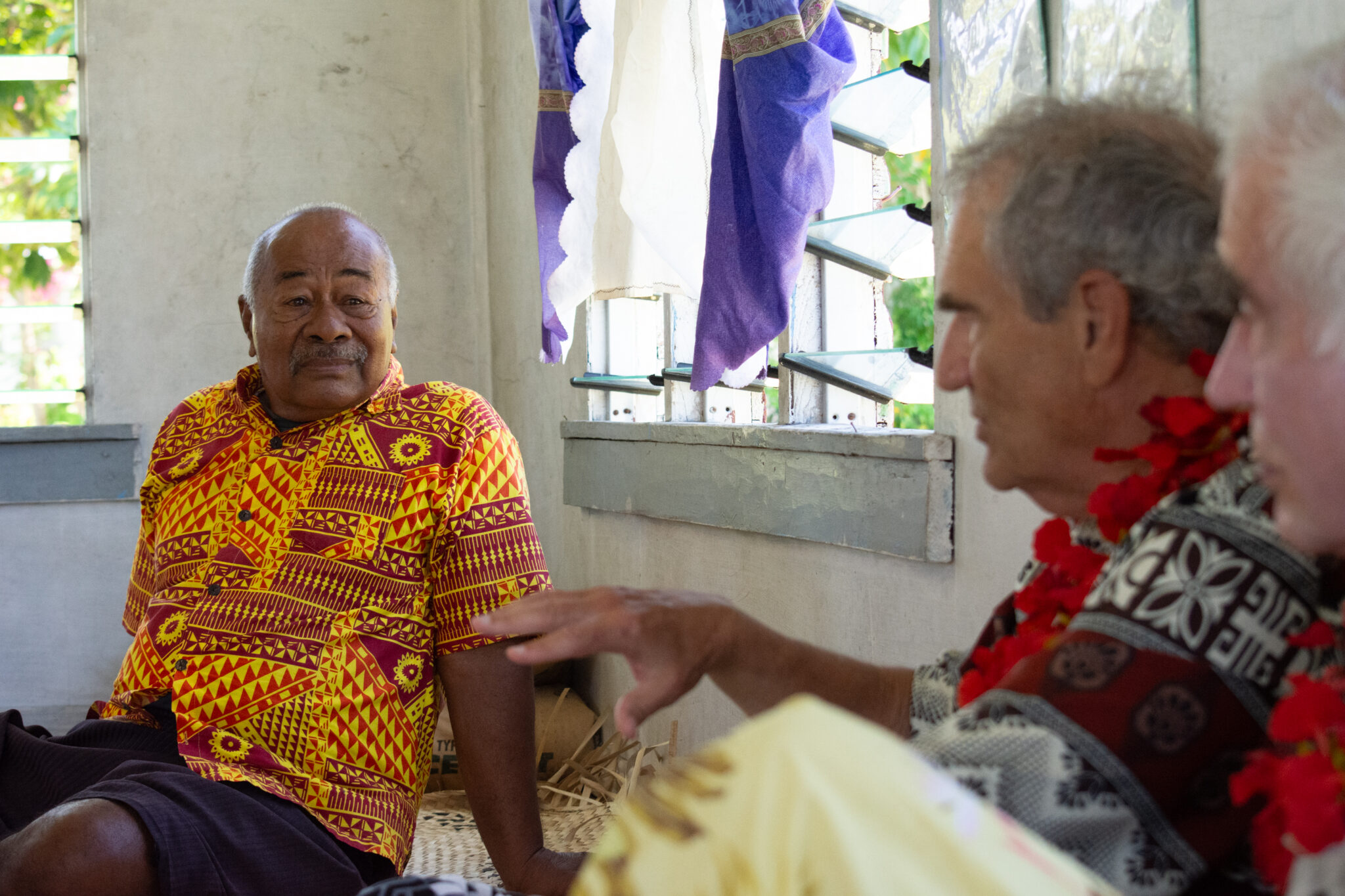 Two men talk while sitting on the floor of the village's meeting hall.